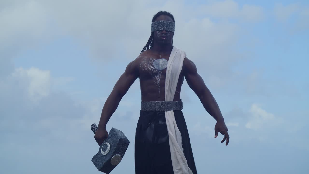 A muscular, dark-skinned man in Nekharis cosplay is deeply immersed in the tropical beach setting