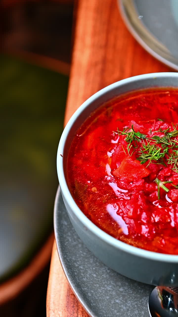 Herb topped red soup serving. Hot red soup garnished with fresh herbs placed beside bread and sauce