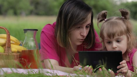 Family-weekend-picnic.-Daughter-child-girl-with-mother-study-lessons-on-tablet.-Distance-education