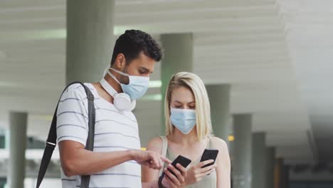 caucasian couple on the go wearing a coronavirus covid19 mask and using phone