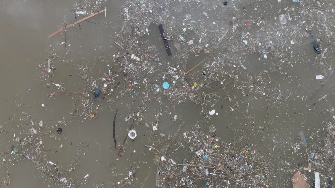 Low altitude aerial drone shot over polluted muddy sewage ocean water and floating trash with debris in Bali Indonesia