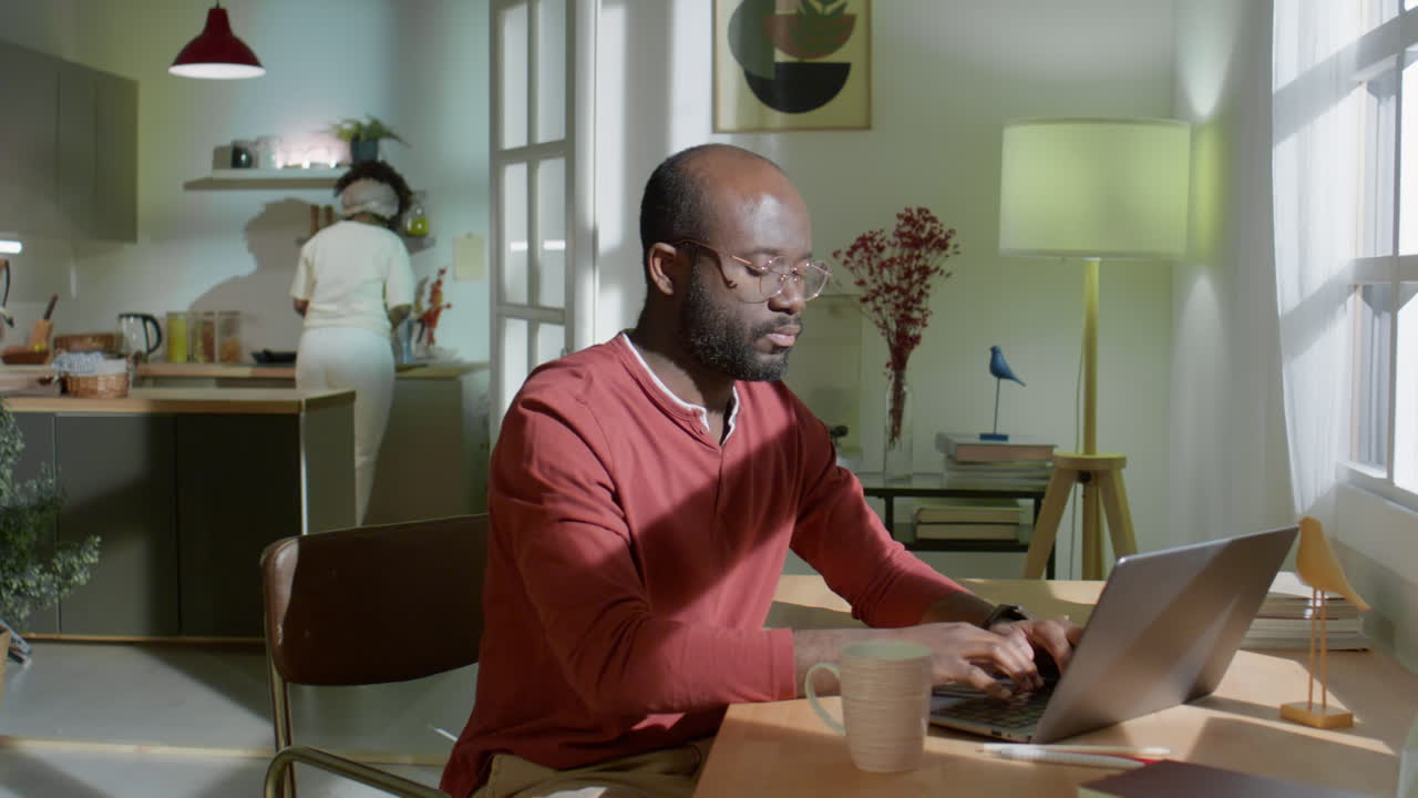 Man Working on Laptop as Wife Cooking Meal at Home
