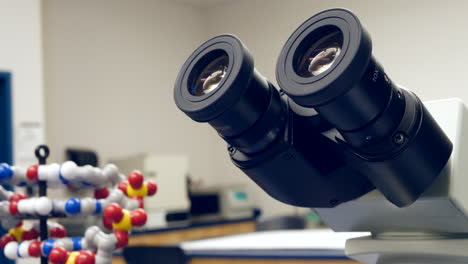 un estudiante en un salón de clases de biología de la universidad haciendo un experimento detrás de un microscopio y un modelo de doble hélice de adn