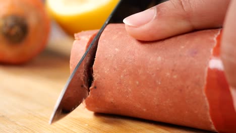 primer plano de una mano cortando un salami en una tabla de madera