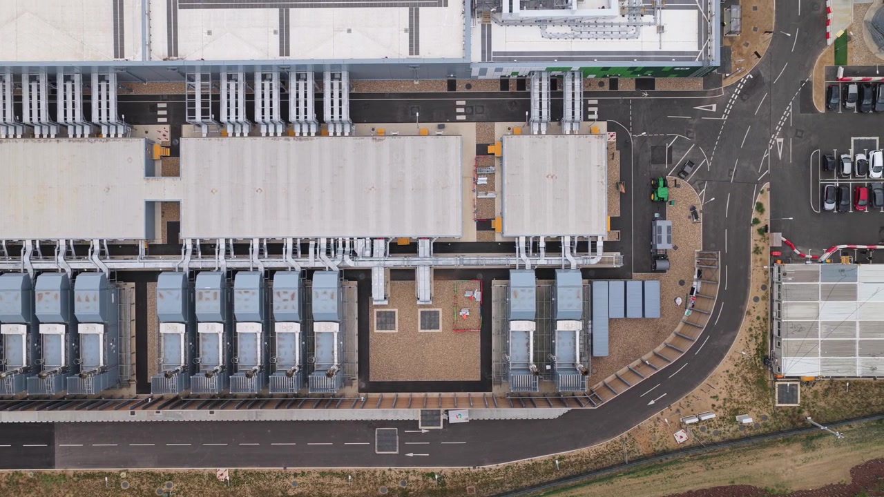 Moderne infrastruktur for cloud computing-faciliteter, der viser tagkølesystemer og parkeringsplads set fra oven i klart dagslys for at repræsentere netværkslagrings- og forbindelsesteknologi