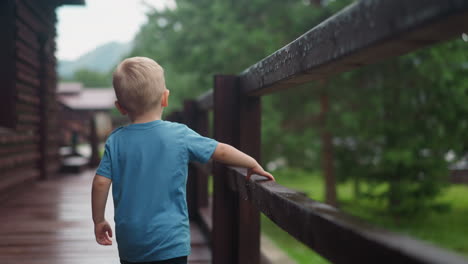 little blond child walks touching wet wooden railing on deck