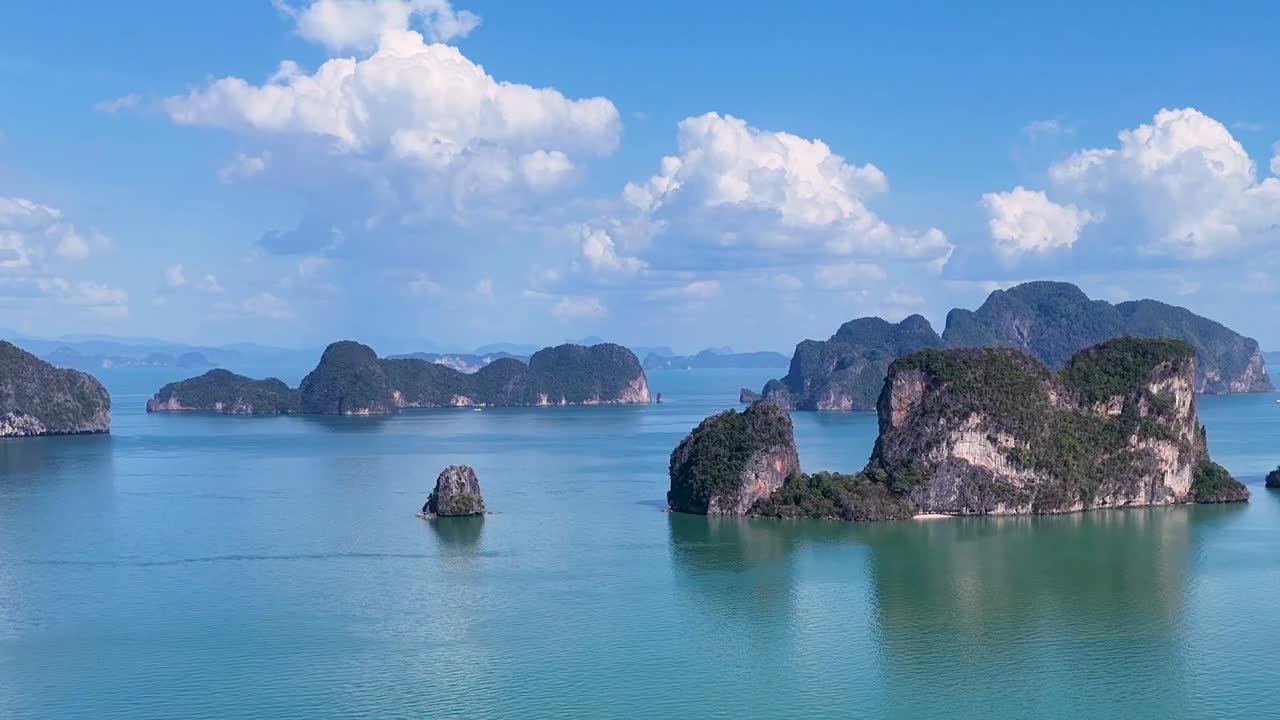 Một chiếc drone bay chậm trên không trung, lướt qua những hòn đảo đá vôi trên làn nước màu ngọc lam tĩnh lặng dưới bầu trời xanh