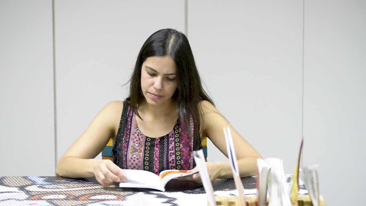 hermosa joven morena leyendo un libro sentado en la mesa