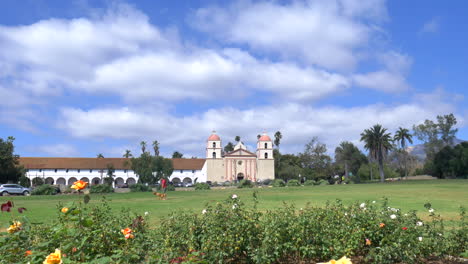 Enthüllen-Sie-Eine-Aufnahme-Des-Kirchengebäudes-Der-Santa-Barbara-Mission-Unter-Blauem-Und-Bewölktem-Himmel-Mit-Blumen-Im-Rosengarten-In-Kalifornien