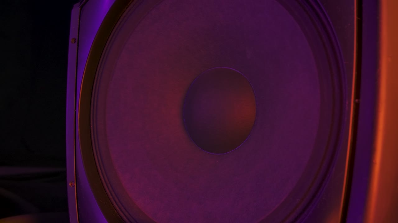 Bass audio speaker during party with colourful lights. Speakers playing and membranes vibrating to the rhythm electronic music. Close up. Slow motion