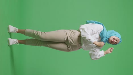 full body of asian muslim woman smiling and dancing while standing in the green screen background studio