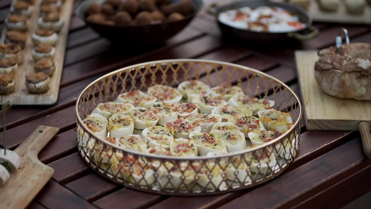 Appetizer rolls topped with herbs and bacon bits displayed in an ornate golden tray