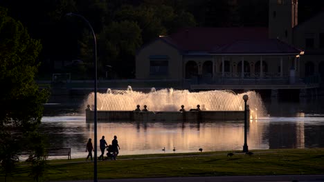 Gente-Caminando-En-El-Parque-De-La-Ciudad-De-Denver,-Colorado-Contra-Un-Fondo-De-Lago-Y-Fuente-De-Agua