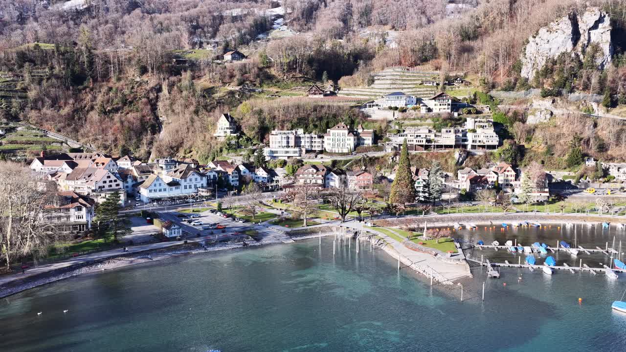 Walensee village in Switzerland with lakeside houses and mountains as drone orbits slowly in bright winter light, calm water, peaceful neighbourhood and alpine landscape