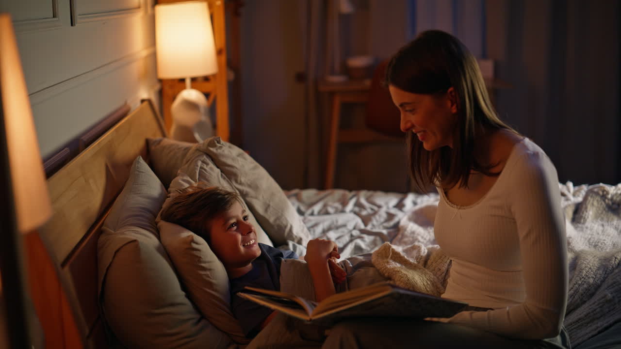 Mommy reading fairy tail happy son lying cozy bed closeup. Mother stroking child