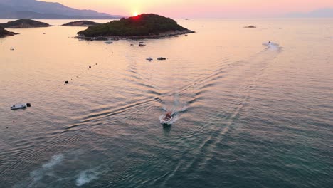 boats speeding through calm waters near ksamil, albania at sunset with scenic islands in view