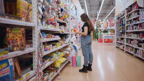 woman holding and inspecting vibrant orange plush purse with green details in well-lit toy store, she carefully examines soft material while shopping, surrounded by colorful toys and shelves filled