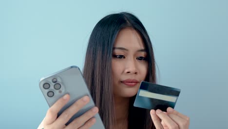 4k 50fps, close-up of a young asian woman holding phone and credit card in hand, filling in credit card information on a mobile phone.