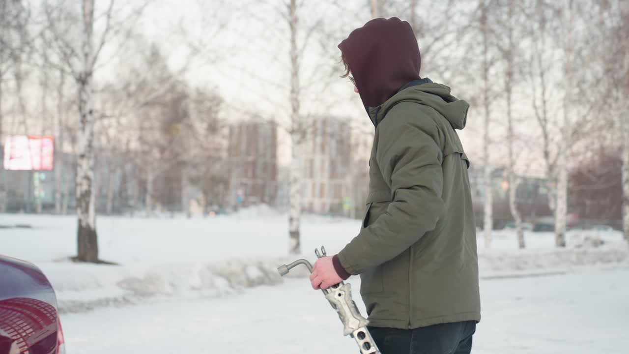 Man finishes work on car, holding spanner and jack, using key to open car boot, dropping tools as winter background sets the scene for car maintenance in cold conditions
