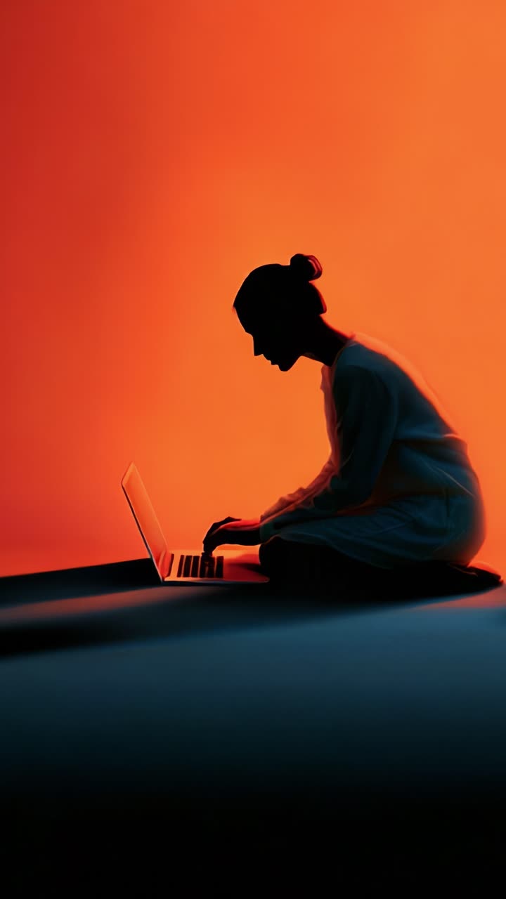 Silhouette of a Person Working Intently on a Laptop Against a Warm Sunset Background Creating a Peaceful and Focused Aesthetic in Orange Tones