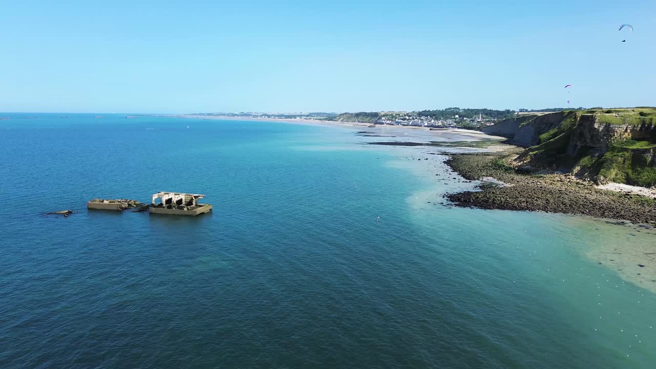 From above, the vestiges of the Arromanches artificial harbour appear in geometric shapes, stretching into the sea