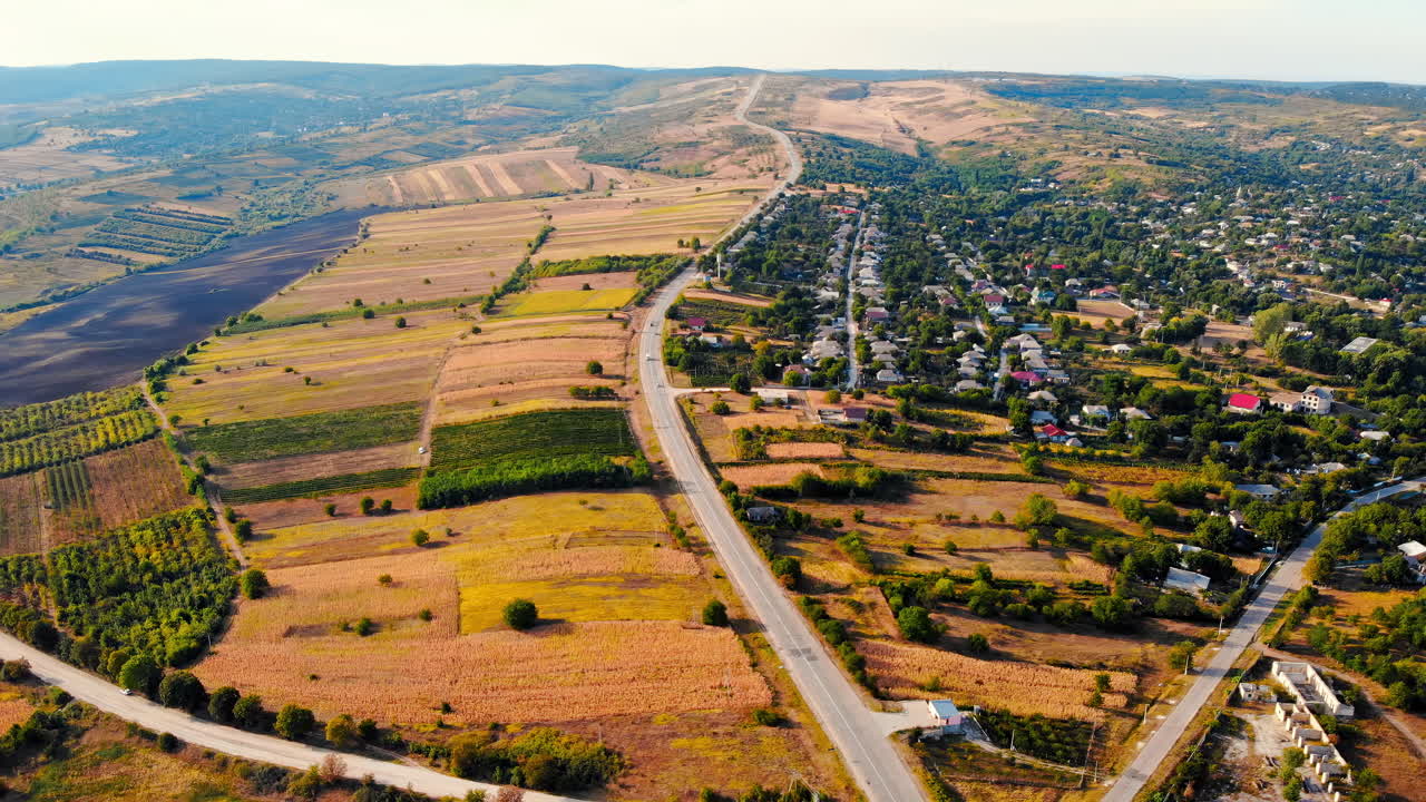 Aerial drone view of a crossroads with moving cars in highland. Small village and green hills on background. Sunny day. Balti, Moldova