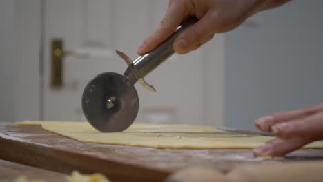 baker cutting flattened dough with pizza cutter