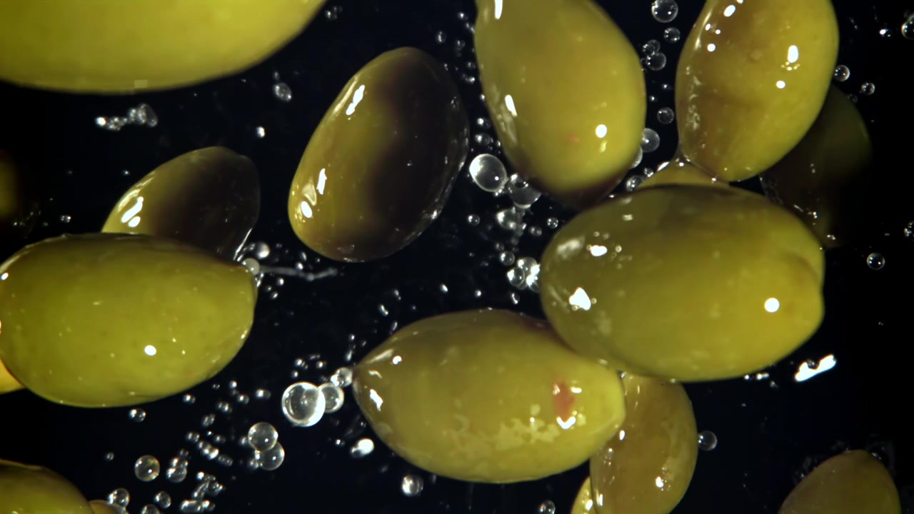 Olive verdi con schizzi d'acqua su sfondo nero al rallentatore