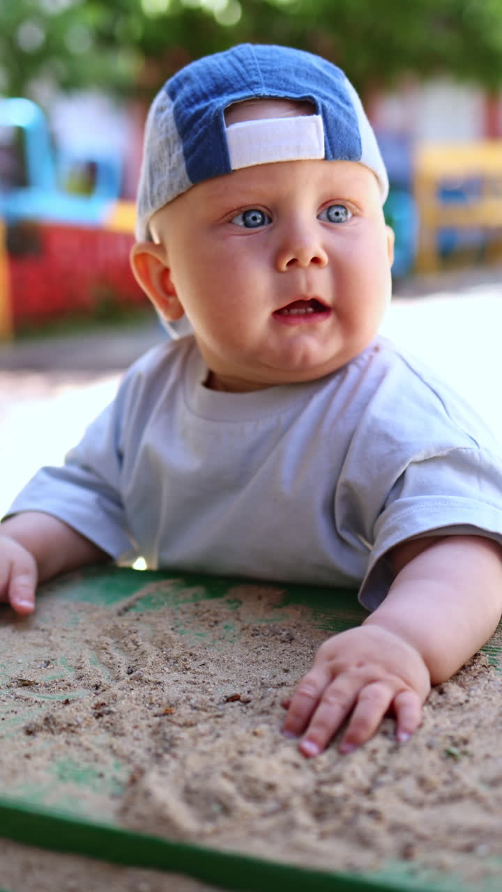 Un bambino con gli occhi azzurri, con un cappello di Panama in testa, gioca nella sabbia. I bambini giocano in una giornata di sole all'aperto con la sabbia.