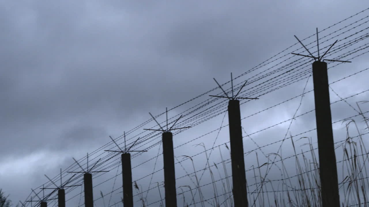 toma panorámica de una valla de alambre de púas de un campo de prisioneros en un día gris y tormentoso