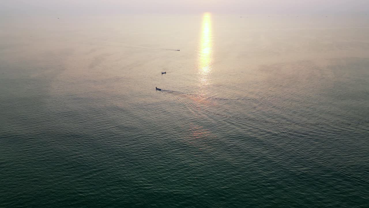 A stunning top drone view of boats scattered across the sparkling blue sea in Goa, India, with the sun casting a golden reflection on the water, creating a peaceful and vibrant coastal scene.