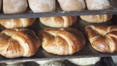 freshly baked croissants and bread cooling on metal baking trays in a bakery