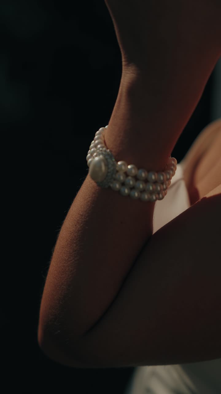 Primo piano del polso della sposa che indossa un braccialetto di perle nella soffusa luce dorata della sera.