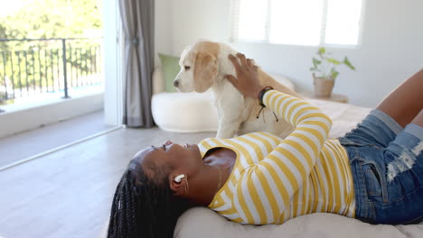 african american young woman lying on bed, petting dog, at home