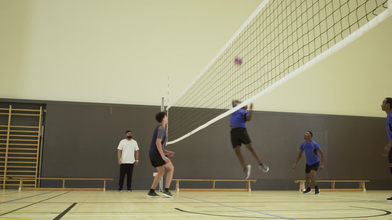 Men's volleyball teams rallying at school gym, blue attacker spiking net to score, blocker jumping