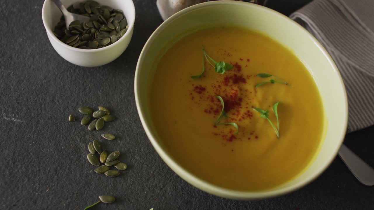video de sopa de verduras con crema en un cuenco en una mesa gris con semillas de calabaza