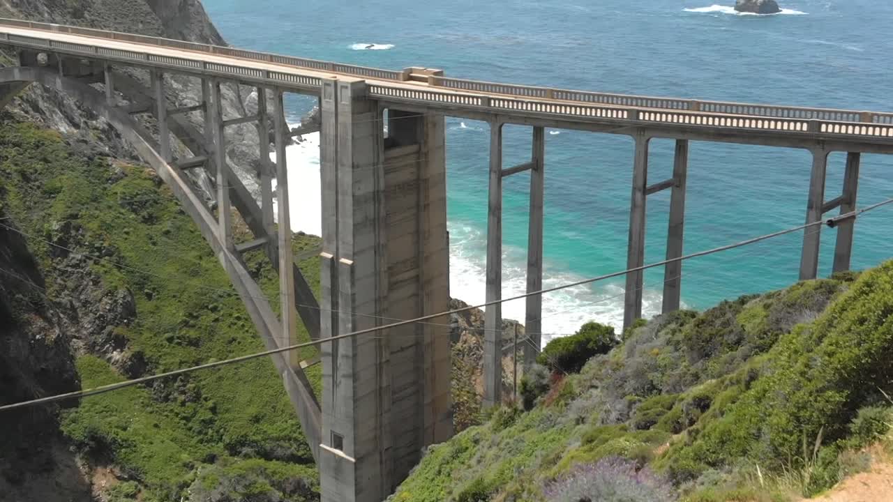 절벽 가장자리에 서서 비크스비 다리를 바라보며 바다를 감상하는 운동선수 소녀의 공중 사진