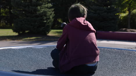 young boy spins around on outdoor play structure on sunny autumn day - medium shot