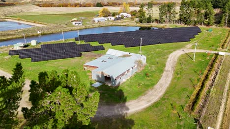 drone footage captures a solar farm surrounded by lush greenery and a reflective pond under clear skies in cromwell