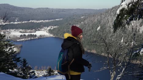 Caucasian-women-sitting-down-in-the-snow-with-a-view-on-Longemer-lake,-in-Vosges,-France