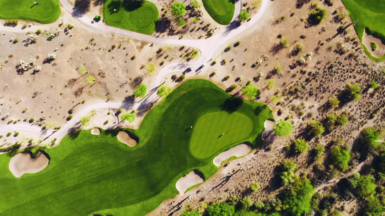 Top-down drone shot of a desert golf green surrounded by sand bunkers with golfers putting
