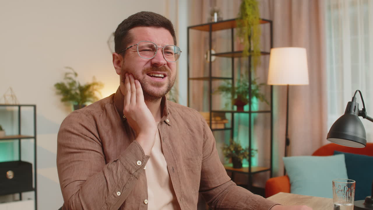 Caucasian young man freelancer sitting at home office table feeling toothache touching mouth at home