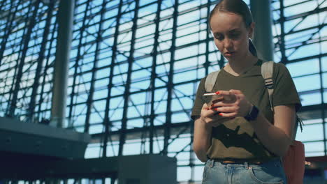 Eine-Reisende-Mit-Rucksack-Steht-Am-Flughafen,-Schaut-Auf-Den-Smartphone-Bildschirm-Und-Tippt-Eine-Nachricht.-Elektronische-Bordkarte-Für-Flugzeug-Und-Zug