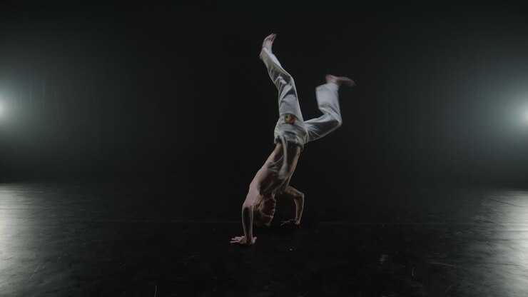 Lottatori di Capoeira che eseguono mosse dinamiche sul palco. Arti marziali, danza e acrobazie in azione. Atleti a torso nudo che mostrano forza, flessibilità e tecnica sotto i riflettori