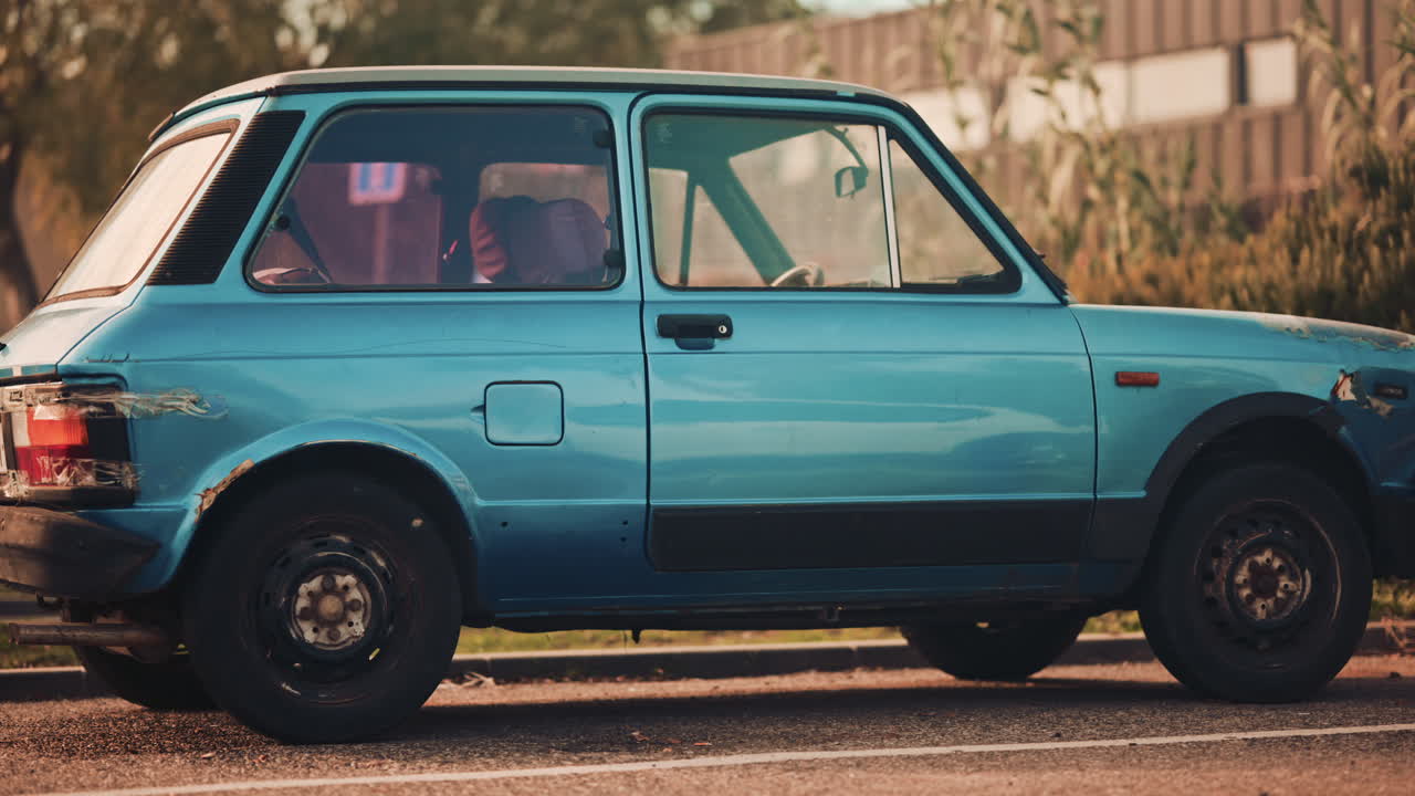 Side view of an old blue compact car with visible wear and rust parked