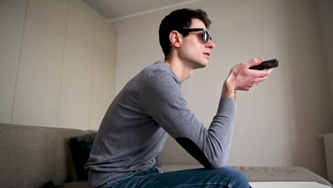 side view of a blind man in sunglasses sitting on the sofa at home while holding a smartphone and having a hands free call