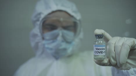 lady doctor wearing protective ppe deep staring at covid 19 vaccine that is in her hand