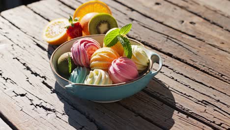 Delicious, colorful scoops of sherbet topped with fresh mint and served with orange, kiwi, and strawberry slices create a refreshing summer dessert on a rustic wooden table