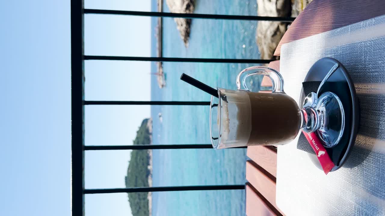 Cup of iced latte with a view of blue sea, rocky coast and the Old Town walls in the background, Dubrovnik, Croatia