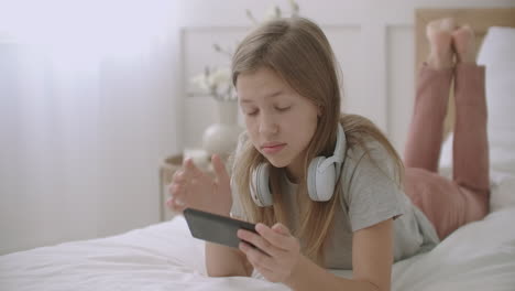 teen girl is lying on bed talking and using app on smartphone chatting online with friends entertainment and leisure of children on vacation and weekend